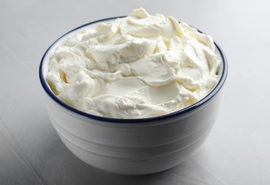 Bowl of tasty cream cheese on grey table, closeup