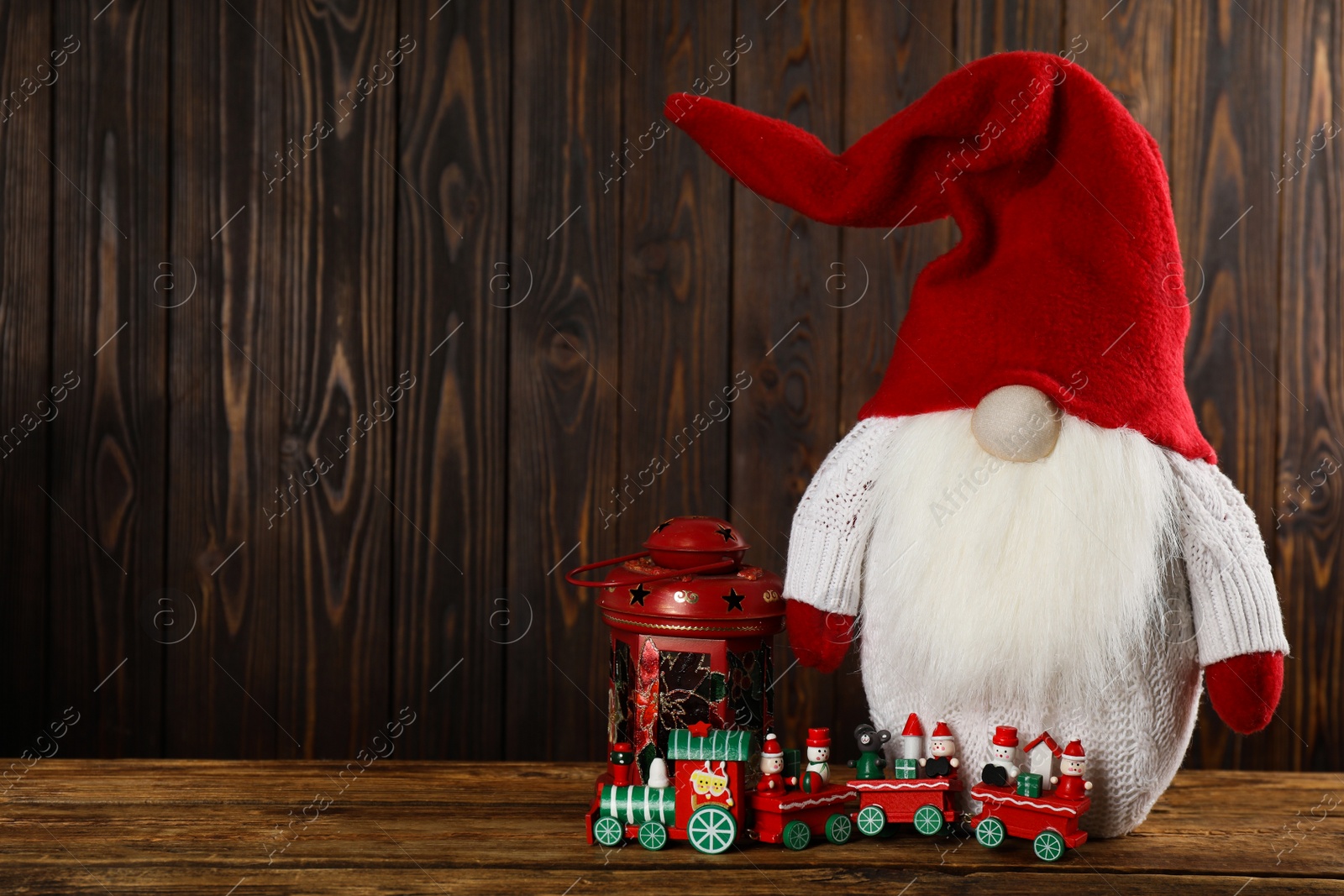 Photo of Cute Christmas gnome, lantern and toy train on wooden table. Space for text