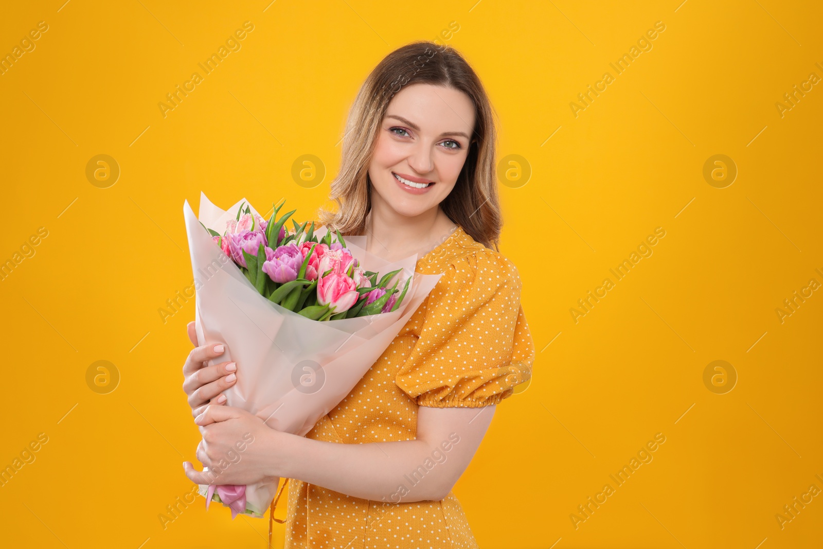 Photo of Happy young woman with bouquet of beautiful tulips on yellow background