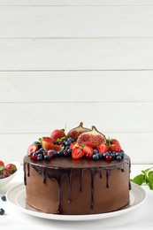 Photo of Fresh delicious homemade chocolate cake with berries on table against wooden background