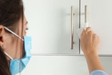 Photo of Woman in medical mask using tissue paper to open cabinet door, closeup