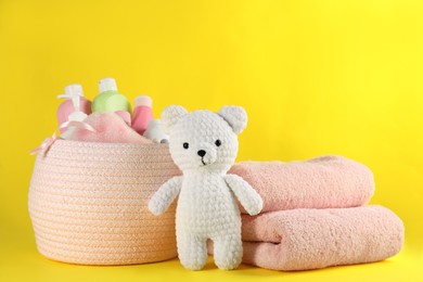 Photo of Basket with baby cosmetic products, toy bear and towels on yellow background