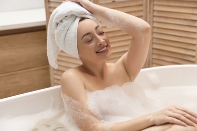 Photo of Happy woman taking bath with foam in tub indoors