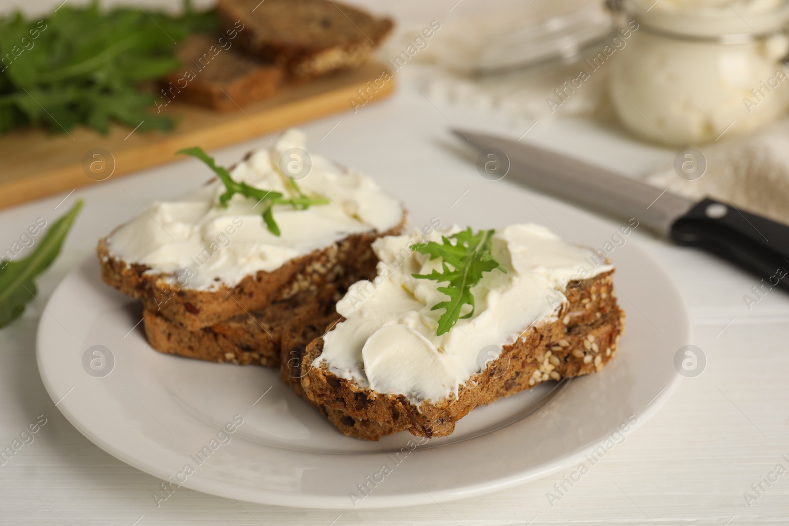 Photo of Bread with cream cheese and arugula on white wooden table