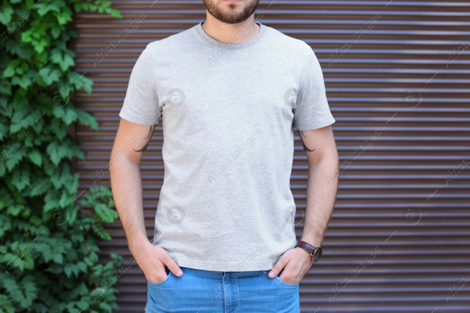 Photo of Young man wearing gray t-shirt near wall on street. Urban style