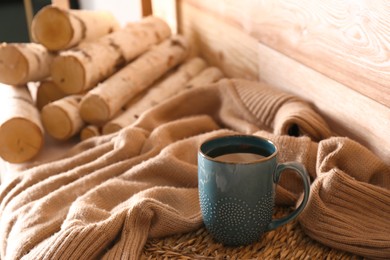 Cup of hot tea and firewood near wooden wall in room. Cozy home atmosphere