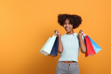 Photo of Happy African American woman with shopping bags on orange background. Space for text