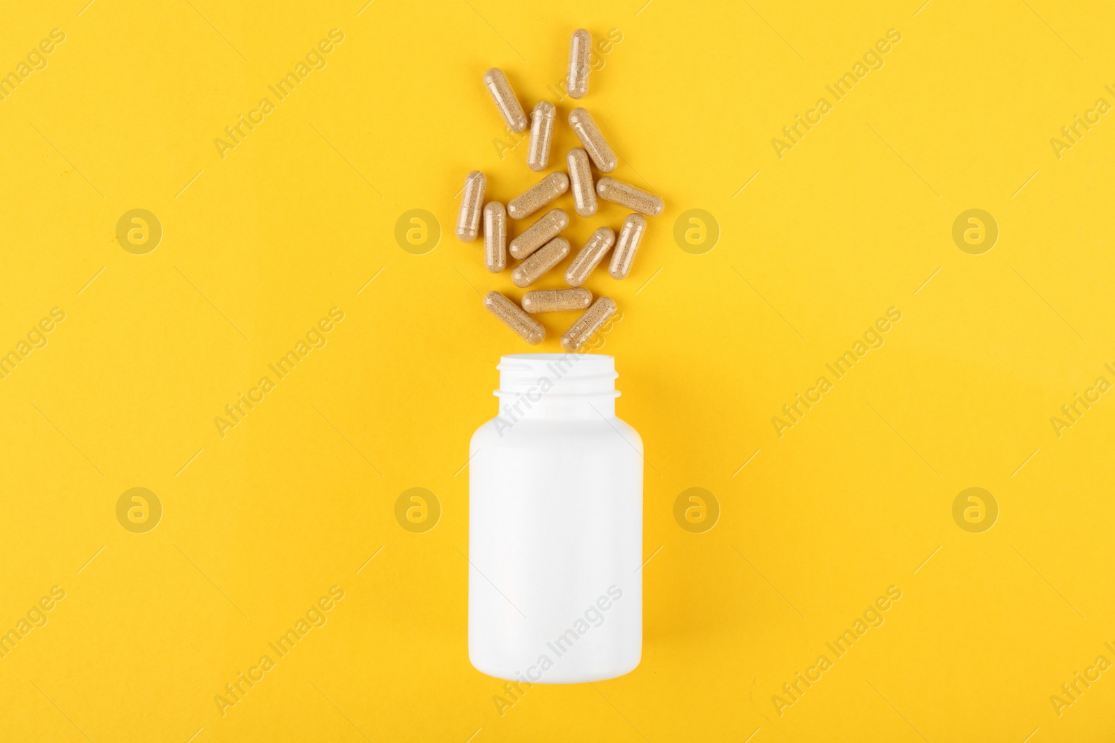 Photo of White medical bottle and vitamin capsules on yellow background, top view