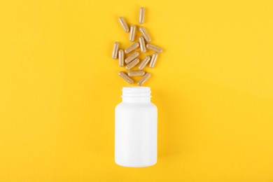 Photo of White medical bottle and vitamin capsules on yellow background, top view