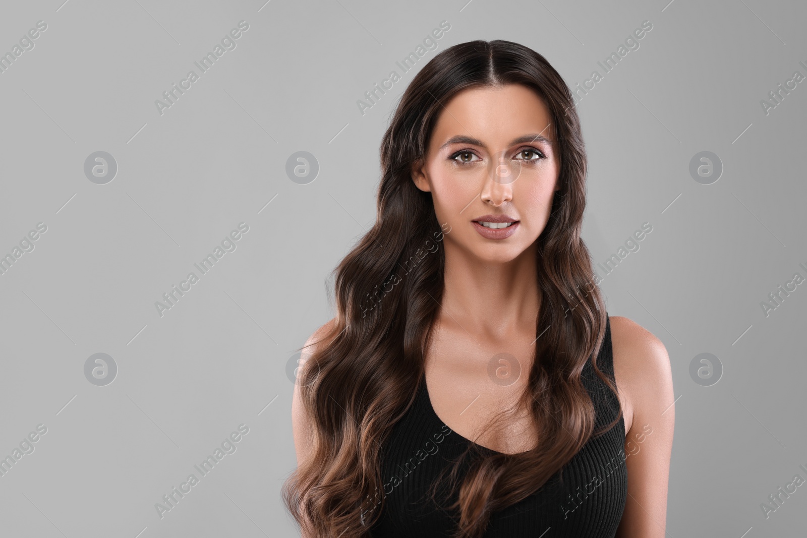 Photo of Hair styling. Portrait of beautiful woman with wavy long hair on grey background, space for text