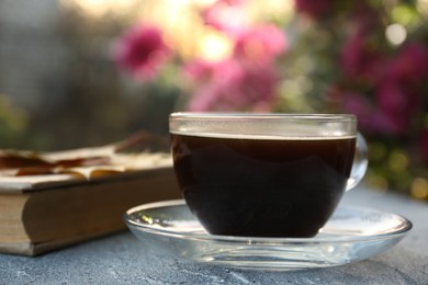 Photo of Glass cup with coffee and book on grey table outdoors, closeup. Morning ritual