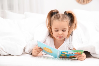 Beautiful little girl with book in bed at home. Bedtime schedule