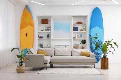 SUP boards, shelving unit with different decor elements and stylish sofa in room. Interior design