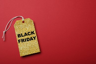 Photo of Golden tag with words Black Friday on red background, top view. Space for text
