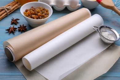 Photo of Rolls of baking parchment paper, different ingredients and kitchen tools on light blue wooden table