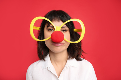Photo of Emotional woman with large glasses and clown nose on red background. April fool's day
