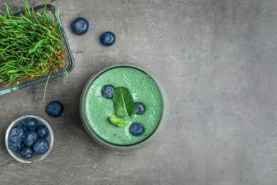Photo of Flat lay composition with spirulina smoothie, wheat grass and blueberries on grey background. Space for text