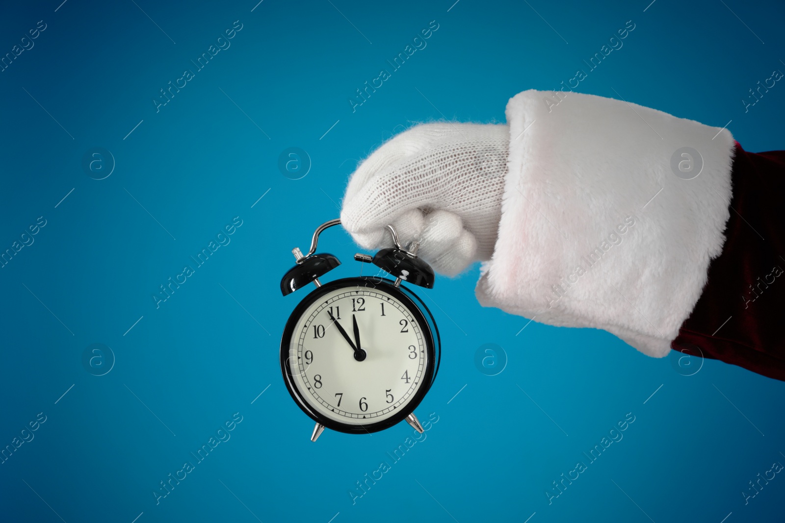 Photo of Santa Claus holding alarm clock on blue background, closeup. Christmas countdown