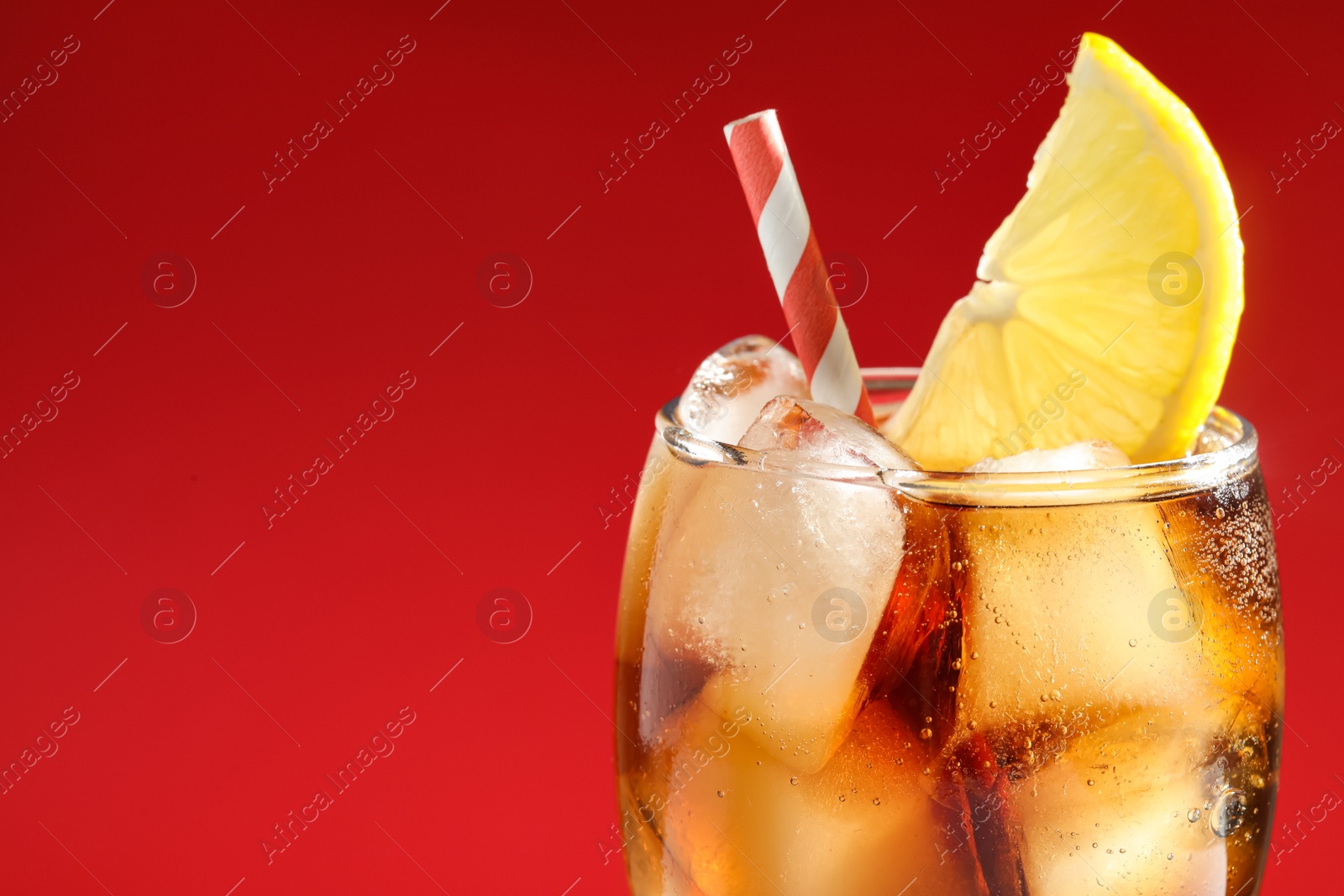 Photo of Glass of refreshing soda drink with ice cubes and lemon on red background, closeup. Space for text