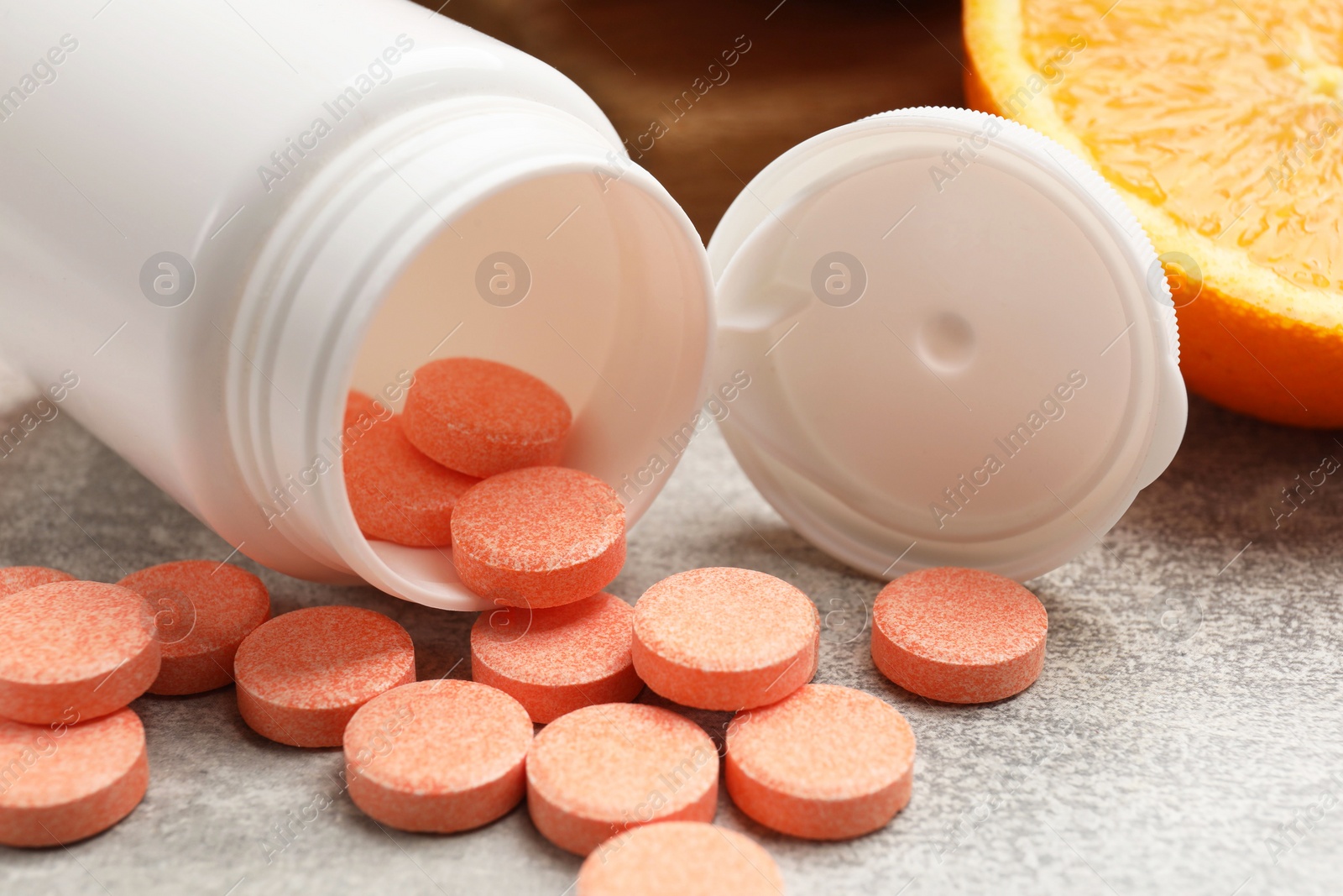 Photo of Dietary supplements. Overturned bottle, pills and orange on grey table, closeup