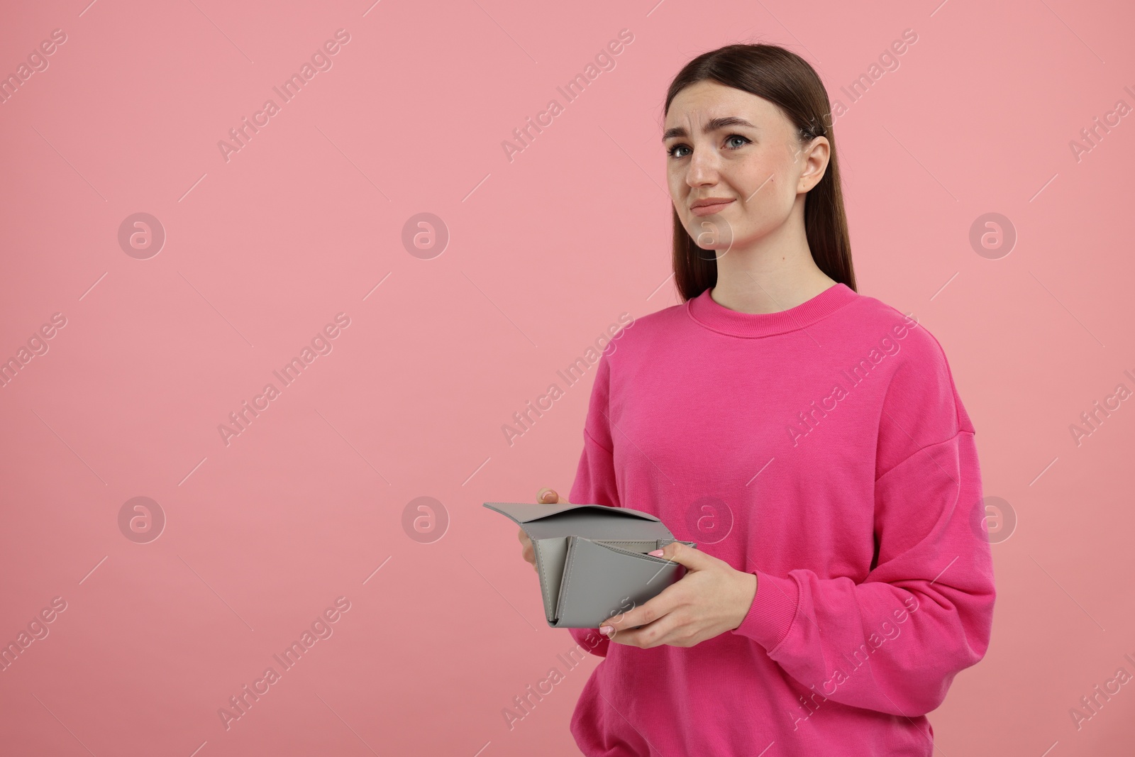 Photo of Sad woman with empty wallet on pink background, space for text