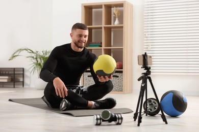 Photo of Trainer with ball streaming online fitness lesson on phone at home