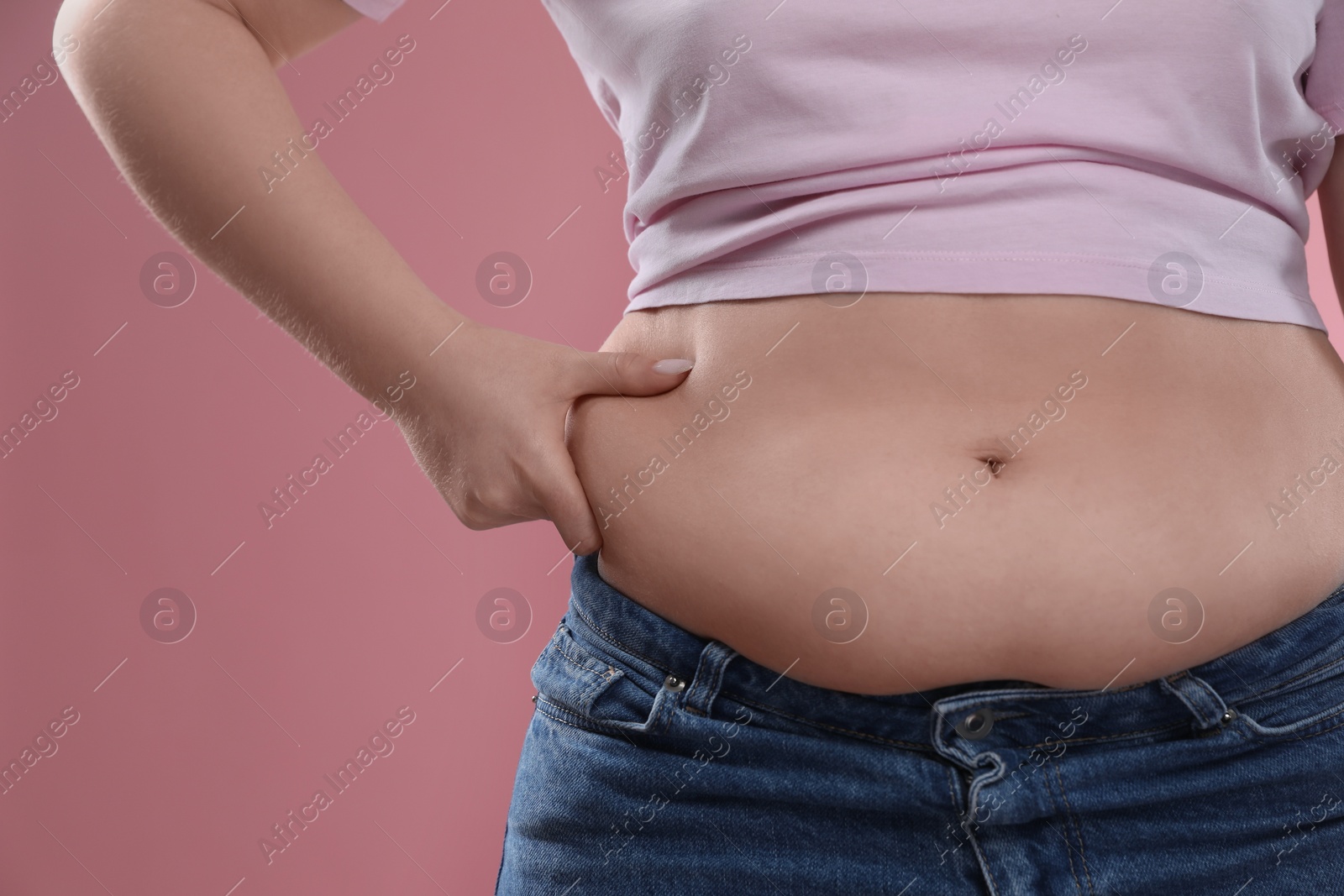 Photo of Woman touching belly fat on pink background, closeup. Overweight problem