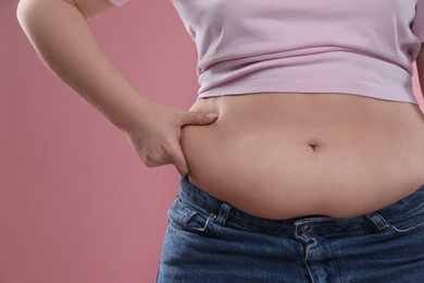 Photo of Woman touching belly fat on pink background, closeup. Overweight problem