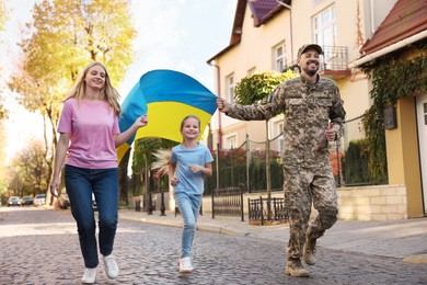 Photo of Soldier in military uniform with his family running and holding Ukrainian flag on city street