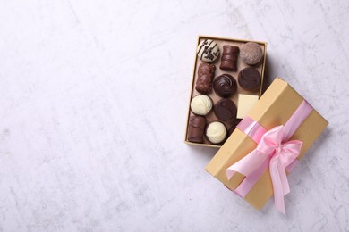 Photo of Open box with delicious chocolate candies on white table, top view. Space for text