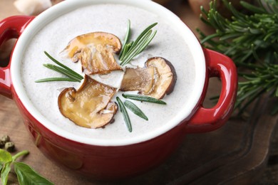 Delicious homemade mushroom soup in ceramic pot and fresh ingredients on wooden table, closeup