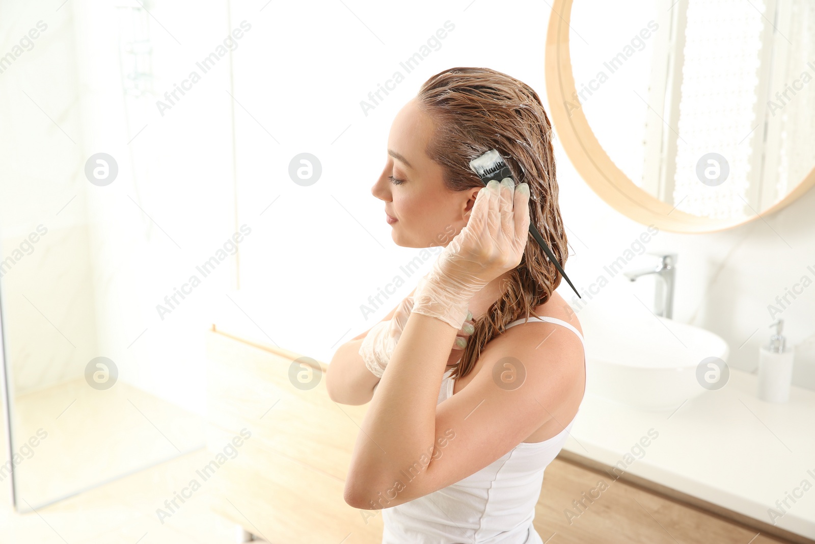 Photo of Young woman dyeing her hair in bathroom