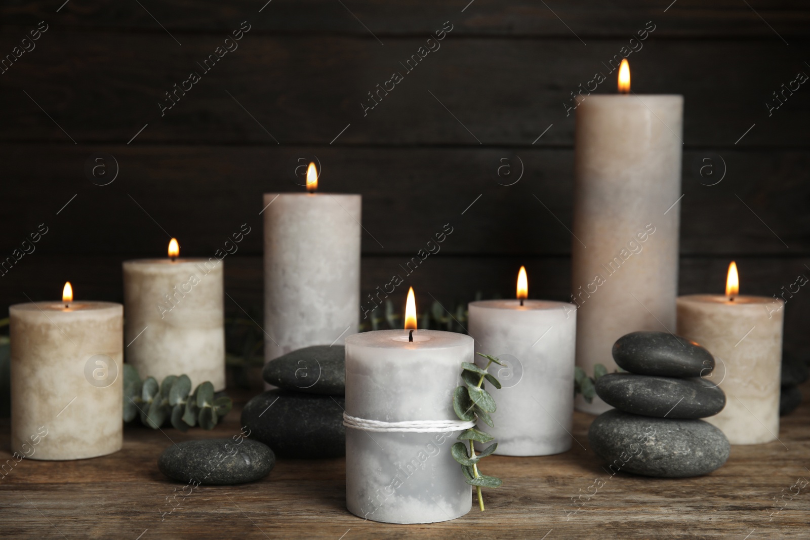 Photo of Composition with burning candles, spa stones and eucalyptus on wooden table