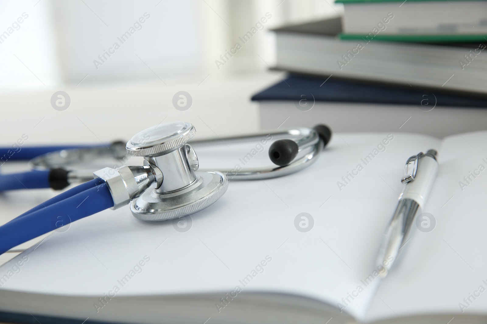 Photo of One new medical stethoscope and books on white table, closeup