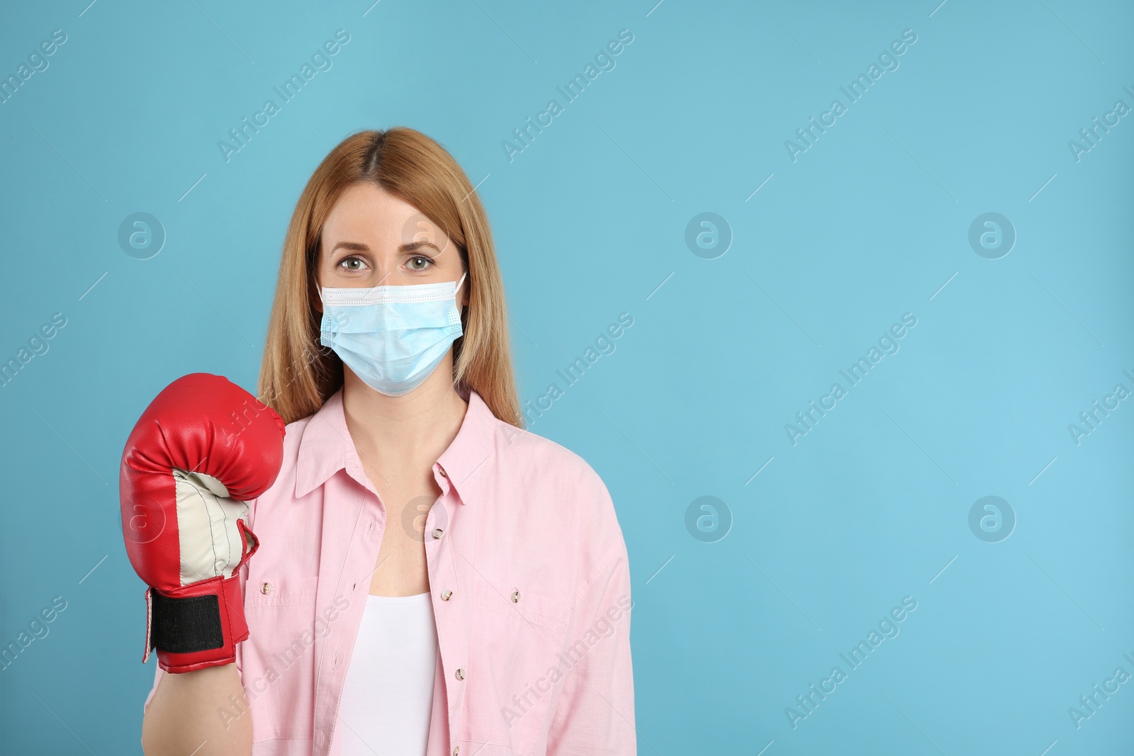 Photo of Woman with protective mask and boxing gloves on light blue background, space for text. Strong immunity concept