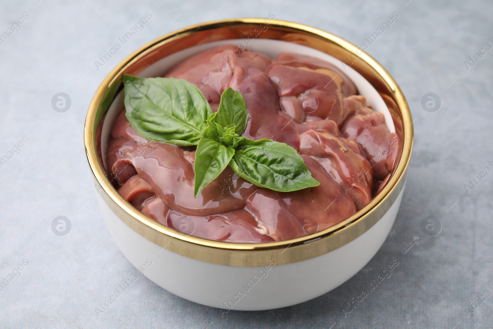 Photo of Bowl with raw chicken liver and basil on light grey table, closeup