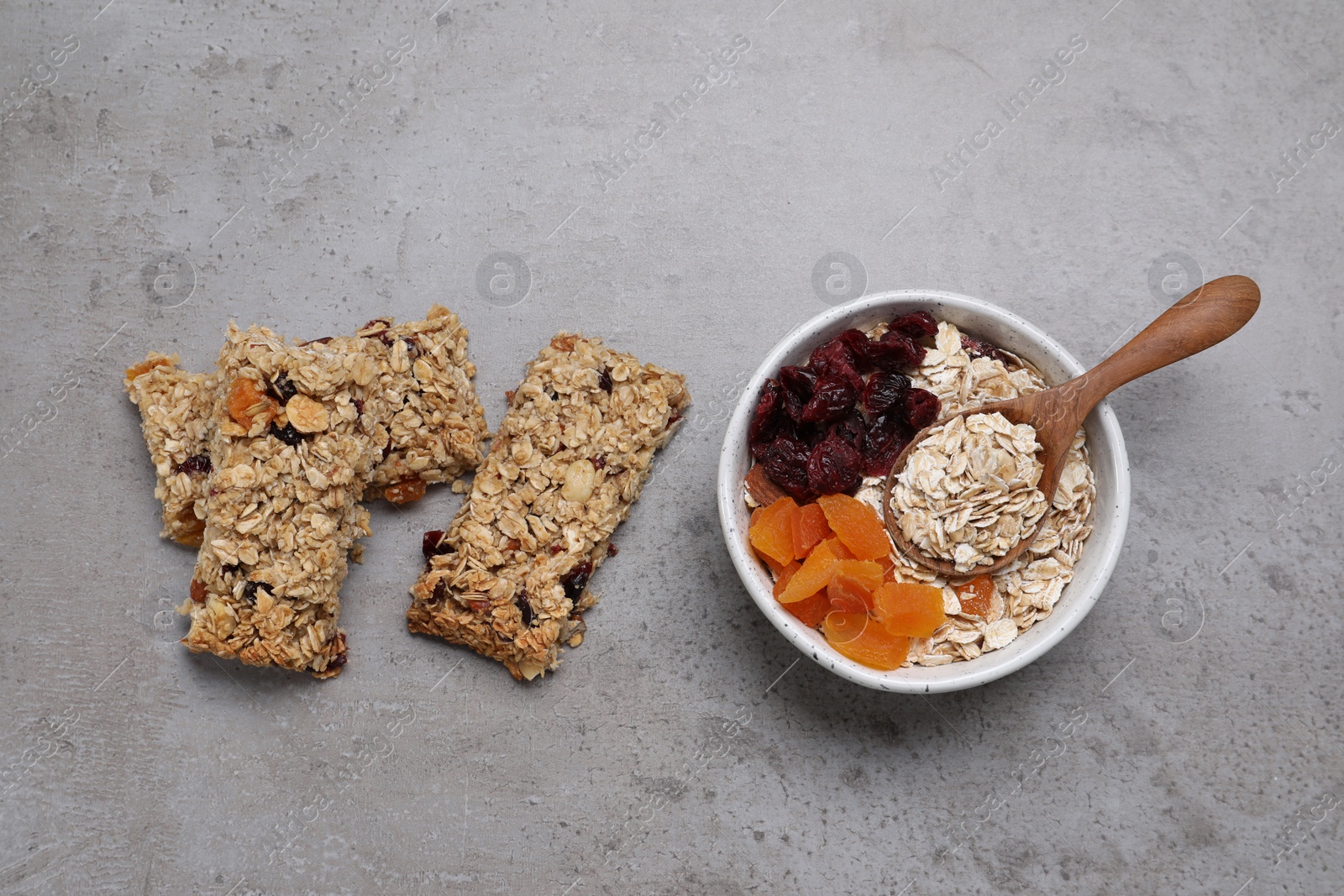 Photo of Tasty granola bars and ingredients on grey table, flat lay