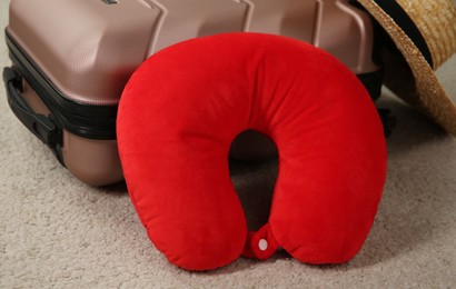 Photo of Red travel pillow and suitcase on beige rug, closeup