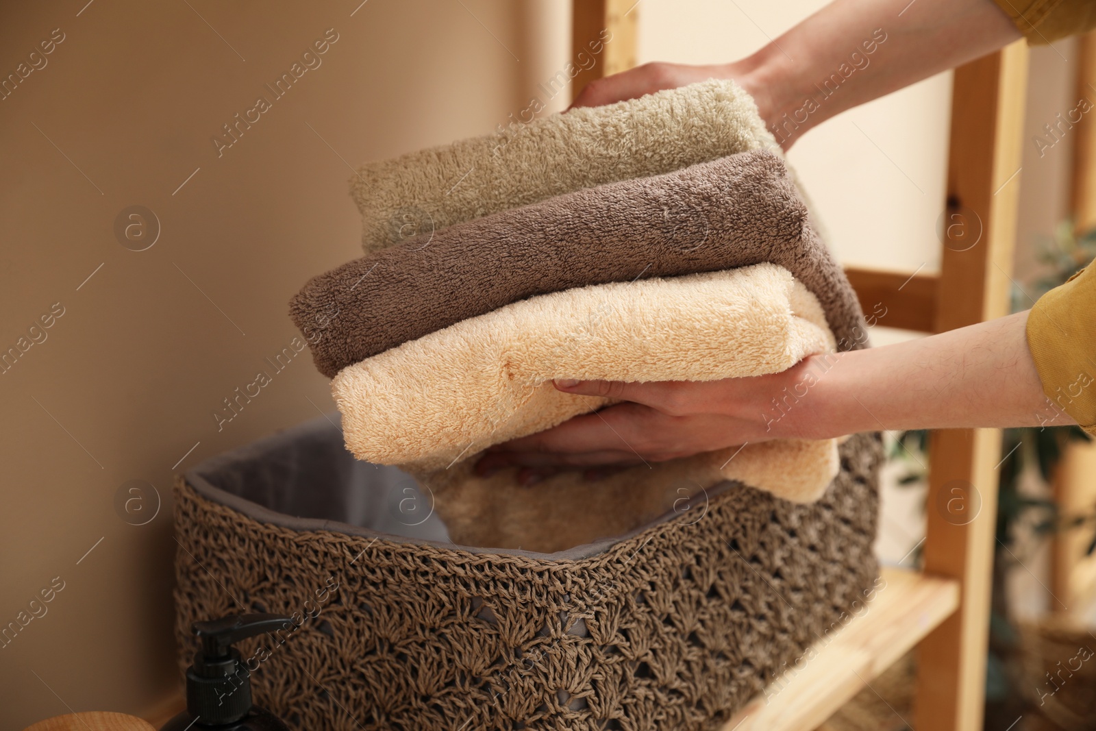 Photo of Woman putting towels into storage basket indoors, closeup