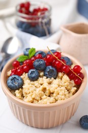 Photo of Bowl of delicious cooked quinoa with blueberries and cranberries on white tiled table, closeup