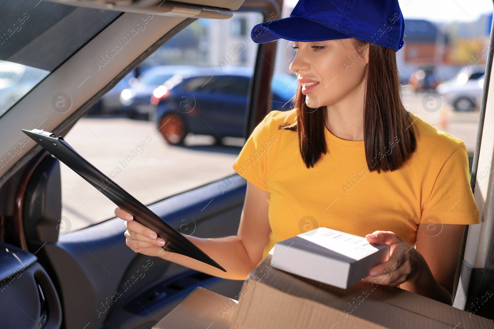 Photo of Courier with clipboard checking packages in car