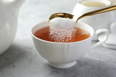 Photo of Adding sugar into cup of tea at grey textured table, closeup