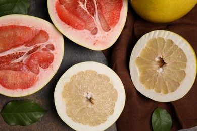 Photo of Fresh cut pomelo fruits with green leaves on dark table, flat lay