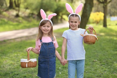 Photo of Easter celebration. Cute little girls with bunny ears holding wicker baskets outdoors