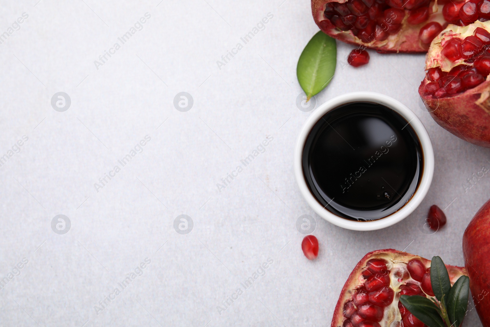 Photo of Tasty pomegranate sauce in bowl, leaves and fruits on light table, flat lay. Space for text