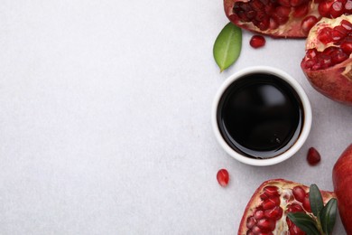 Photo of Tasty pomegranate sauce in bowl, leaves and fruits on light table, flat lay. Space for text