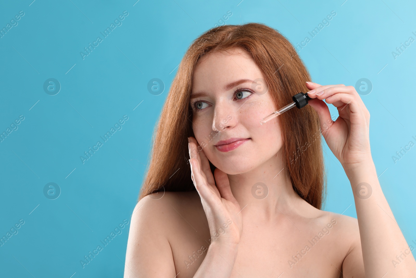 Photo of Beautiful woman with freckles applying cosmetic serum onto her face against light blue background. Space for text