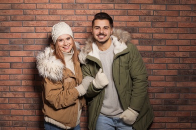Young couple wearing warm clothes against brick wall. Ready for winter vacation