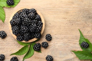 Ripe blackberries and green leaves on wooden table, flat lay. Space for text