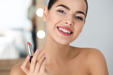 Photo of Young woman applying lipstick on blurred background